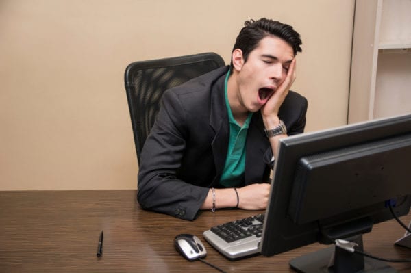 Tired bored young businessman sitting in office yawning