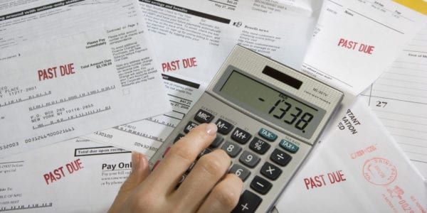 Woman using calculator on desk full of bills and statements, close-up of hand